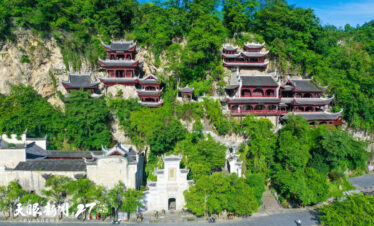 ancient architecture group of tsing lung hole, guizhou, china tour, Cliffside temple complex with stacked red pagodas rising among green trees and a stone gate at the base.
