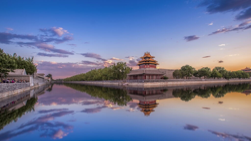 forbidden city, beijing, chinatrip, Traditional red and gold Chinese pagoda on a stone platform beside a calm lake, sunset sky and trees reflected in the water.
