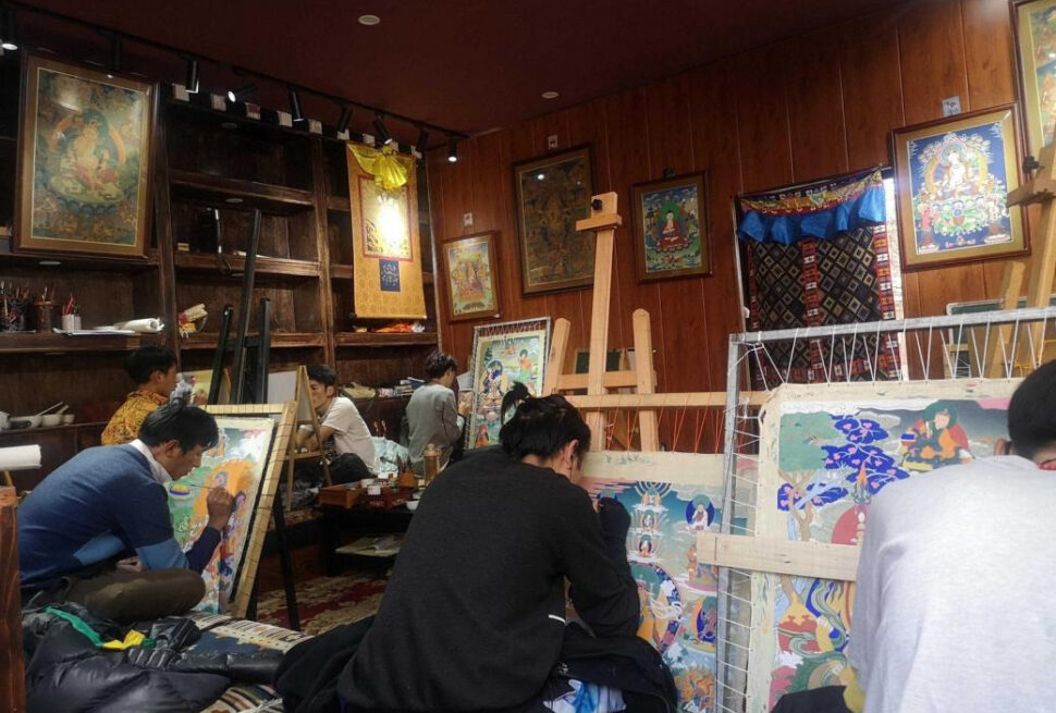 Tangka, Tibet, chinattrip, Artists in a wood-paneled studio painting large colorful canvases on easels, with many framed artworks hanging on the walls.