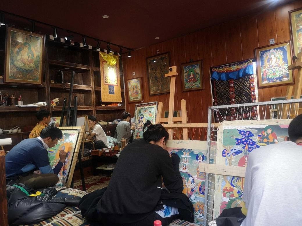 Tangka, Tibet, chinattrip, Artists in a wood-paneled studio painting large colorful canvases on easels, with many framed artworks hanging on the walls.