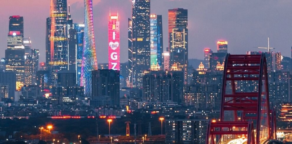 guangzhou, chinatrip, Nighttime city skyline with illuminated skyscrapers and a red bridge in the foreground.