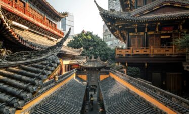 Luohan Temple, Arhat Temple, chongqing, chinatrip, Traditional Chinese temple rooftops with ornate wooden carvings and a narrow stone path in the courtyard, city skyscrapers in the background