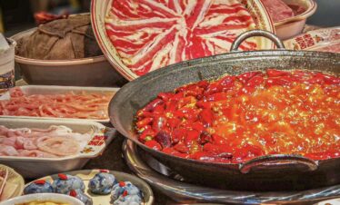 Hotpot, chongqing day tour, chinatrip, Large hot pot with a fiery red broth and chopped chilies, surrounded by raw meats and side dishes for a communal meal.
