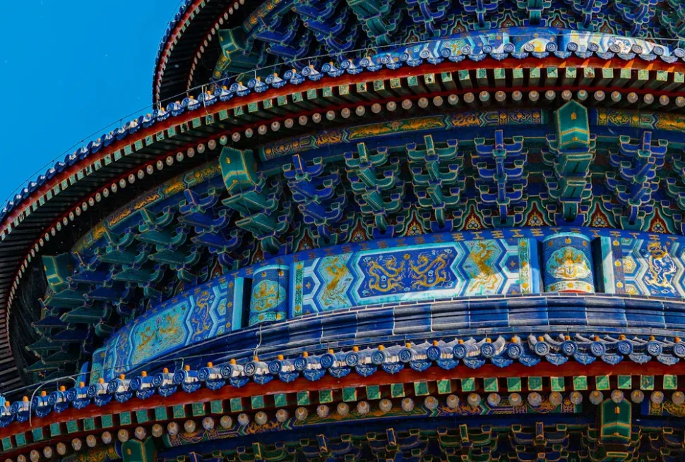 temple of heaven, beijing, chinatrip, Close-up of a traditional Chinese pagoda roof with blue-green tiles and intricate painted patterns against a blue sky.