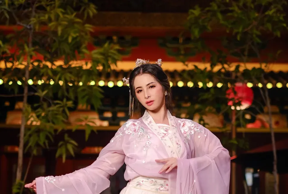 hanfu photoshoot, guizhou, female, solo, chinatrip, Woman in a pink embroidered hanfu with flowing sleeves performing a traditional dance at night outdoors.