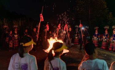 School trip in Guizhou, chinatrip, Group of people in colorful traditional costumes standing around a blazing bonfire at night, sparks flying from the flames.