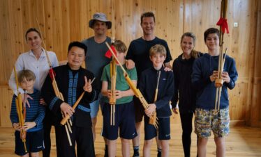 School trip in Guizhou, chinatrip, Group of nine people in a wood-paneled room holding bamboo wind instruments and smiling at the camera.