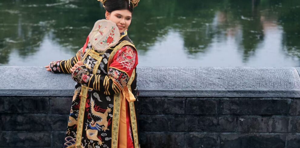 hanfu photoshoot, the forbidden city, beijing, qing dynasty, female, solo, chinatrip, Woman in an ornate Chinese imperial costume with dragon embroidery, standing by a stone railing beside a calm, green pond