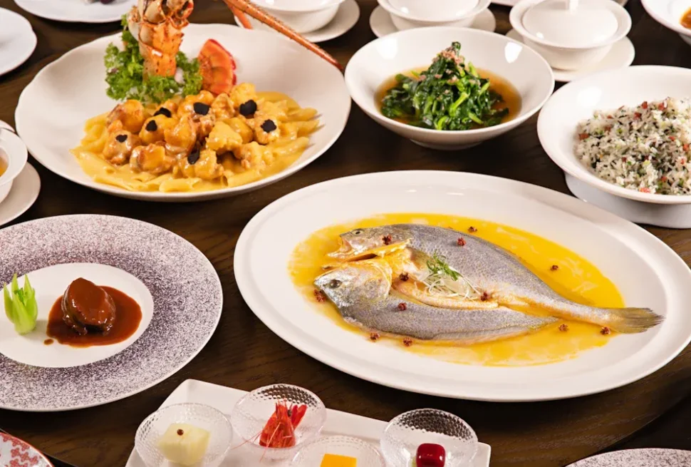 chinese food, chinatrip, Assorted fine-dining dishes on a table, featuring a whole fish in yellow sauce, a seafood pasta, greens, rice, and a dessert plate.