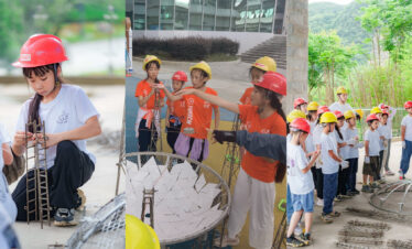 school trip china guizhou, chinatrip, Group of children in orange and white shirts wearing red and yellow hard hats collaboratively assembling a wire-frame sculpture outdoors.