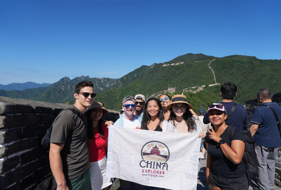 CET Marketing Team,Chinatour Group of diverse tourists on the Great Wall of China holding a white banner reading China Explorer Tour, smiling at the camera.