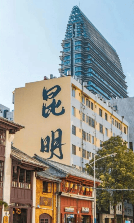 Kunming,Chinatour City street with traditional storefronts in the foreground, a beige building displaying two large black Chinese characters on its side, and a tall modern skyscraper in the background.
