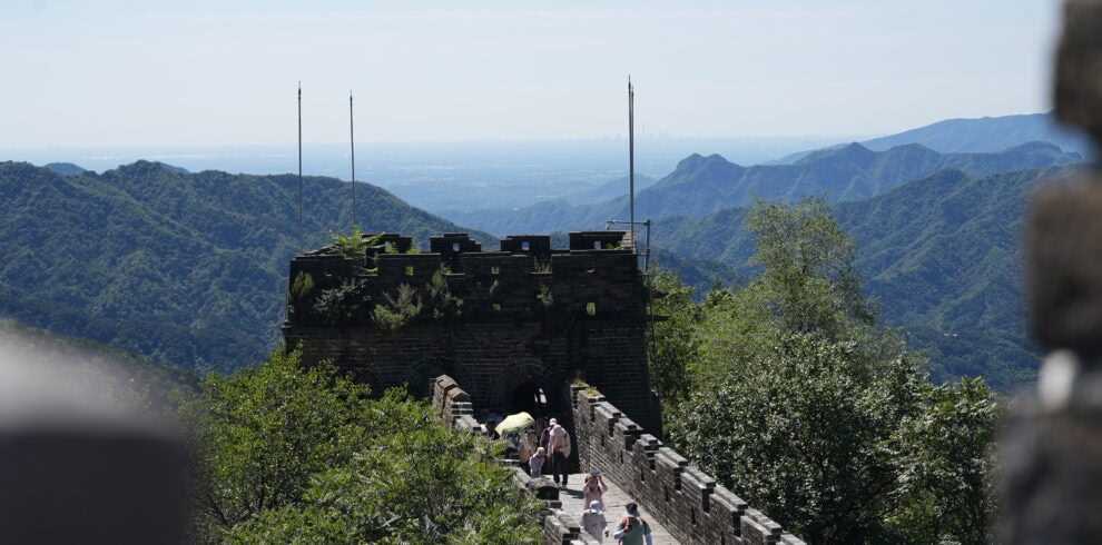 Section of the Great Wall winding through green mountains with visitors walking along the crenellated walkway