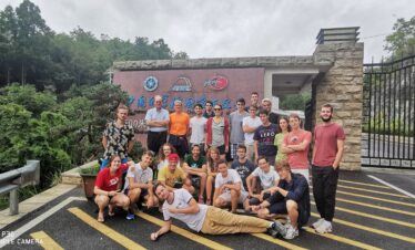 guizhou's FAST, chinatrip, A large group of students and a few adults posing for a group photo outside an institute entrance sign, with greenery and a black metal gate in the background.
