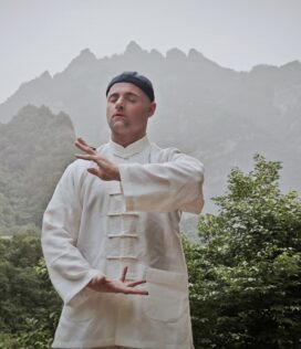 taichi wudang, hubei, chinatravel, Martial artist in a white traditional outfit performing a Tai Chi pose in a misty mountainous forest setting.