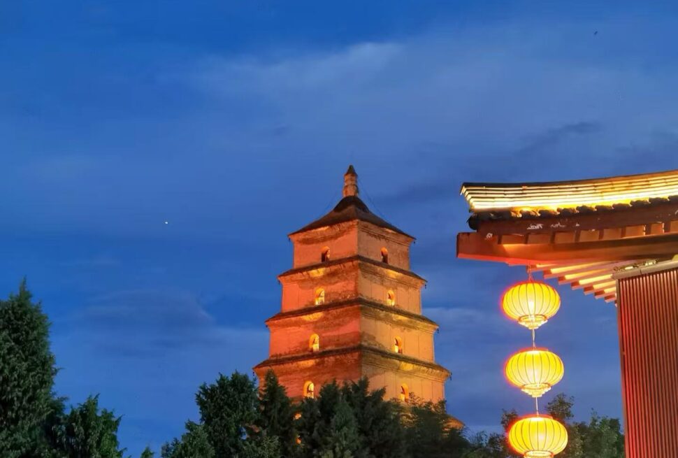 Brick pagoda tower lit at dusk with a blue sky and hanging red lanterns to the right.