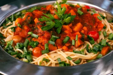 Spaghetti topped with tomato sauce and chopped greens in a metal bowl, garnished with parsley and green onions.