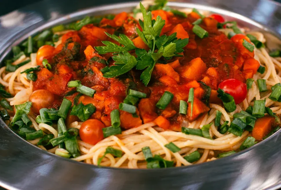 Spaghetti topped with tomato sauce and chopped greens in a metal bowl, garnished with parsley and green onions.