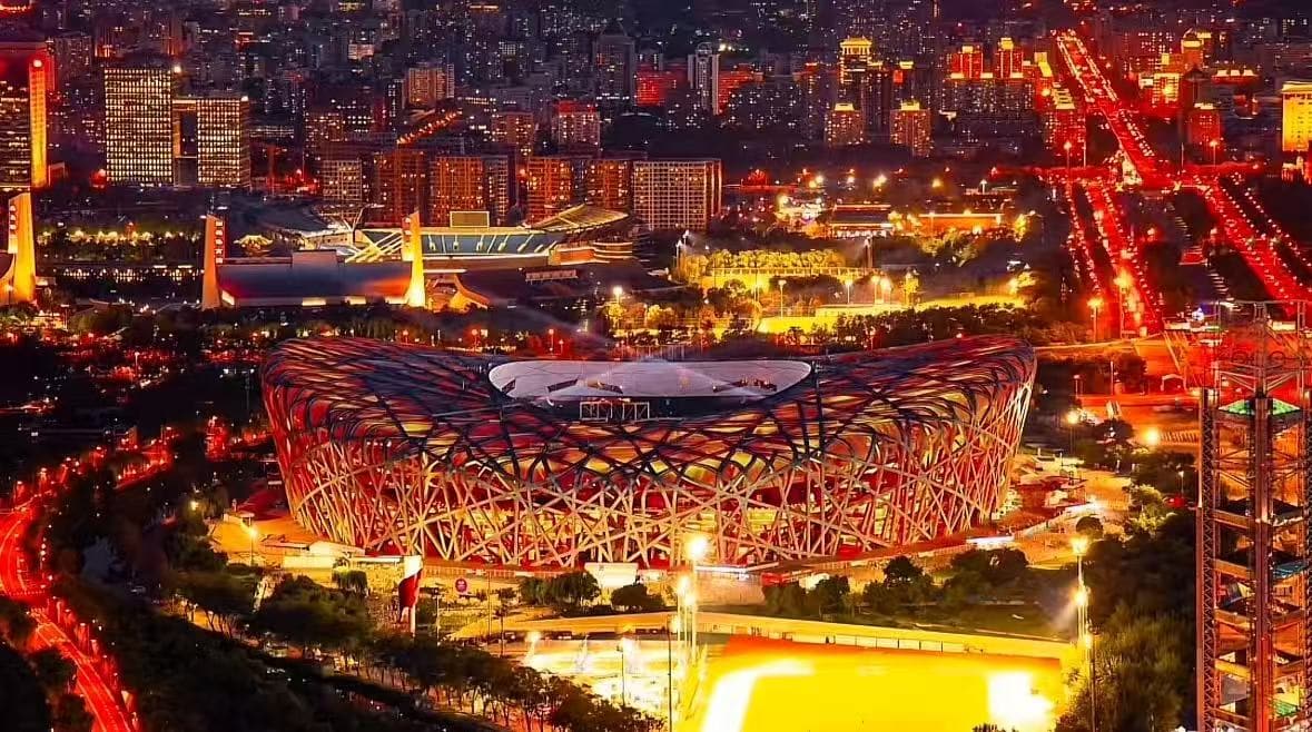 Olympic Forest Park,Beijing,Chinatour Night aerial view of the Beijing National Stadium (Bird's Nest) illuminated in red and orange, with city lights in the background.