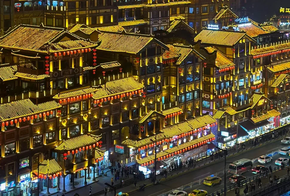 Night view of a block of traditional Chinese buildings with yellow-tiled roofs and red lanterns along a busy street at night.