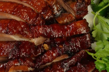 Glazed sliced barbecue pork arranged on a plate with fresh cilantro on the side.