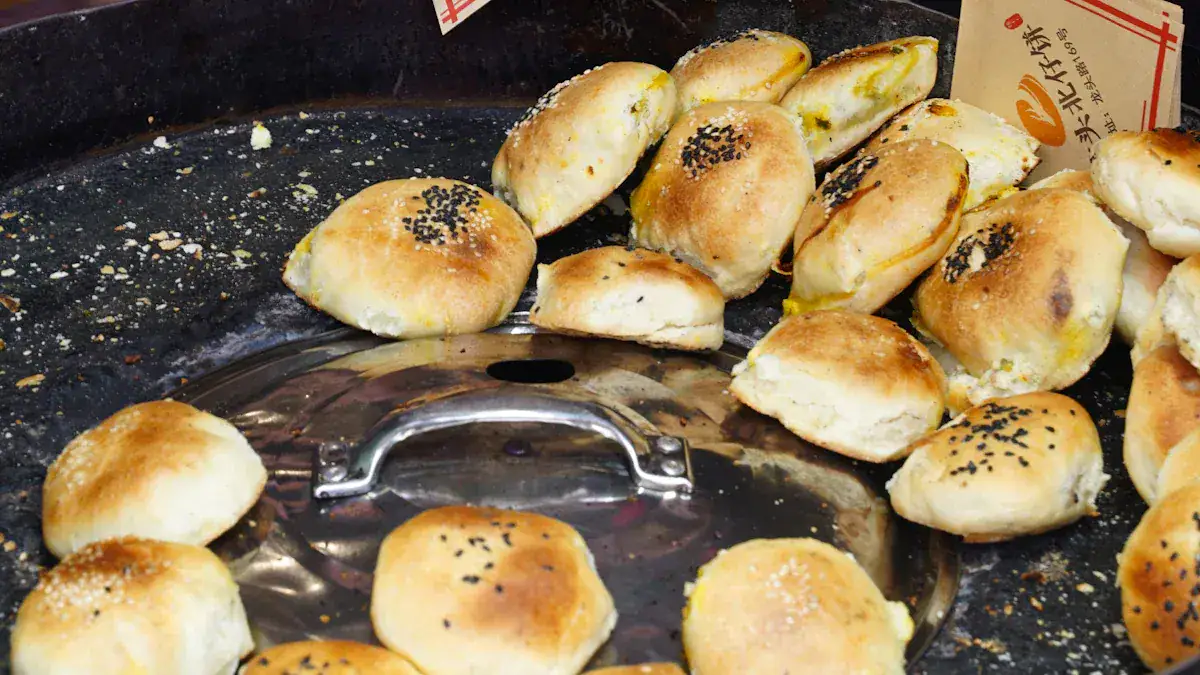 Round golden-brown buns surrounding a shiny metal lid on a dark baking surface, some topped with sesame seeds.