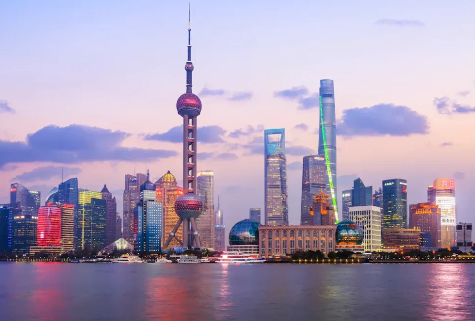 Evening skyline of Shanghai along the Huangpu River, featuring the illuminated Oriental Pearl Tower and futuristic skyscrapers.",