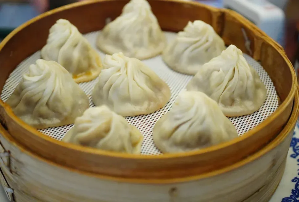 Steamer basket with eight steamed dumplings arranged in a circle, pale dough folds on top.