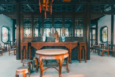 Dark wood shrine room with an ornately carved altar, porcelain vases, and a round marble-topped table.