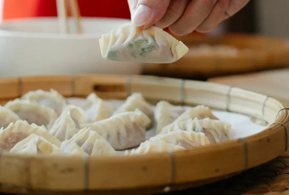 Bamboo steamer filled with steamed dumplings as a hand lifts one up with chopsticks.