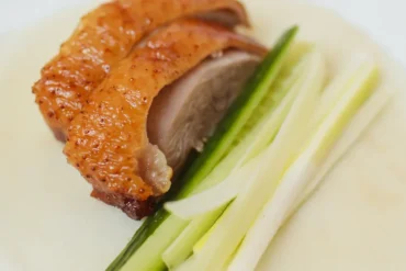 Crispy-skinned roasted chicken leg served on a bed of cucumber sticks with a pale sauce on a white plate.