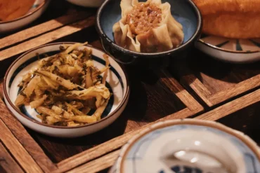 Steamed dumpling in a dark bowl with a shredded vegetable side on a wooden table.