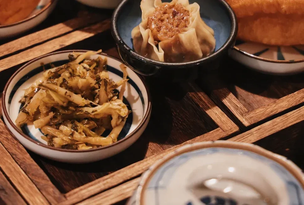 Steamed dumpling in a dark bowl with a shredded vegetable side on a wooden table.