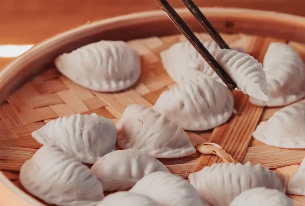 Dumplings arranged in a bamboo steamer, with chopsticks lifting one dumpling.