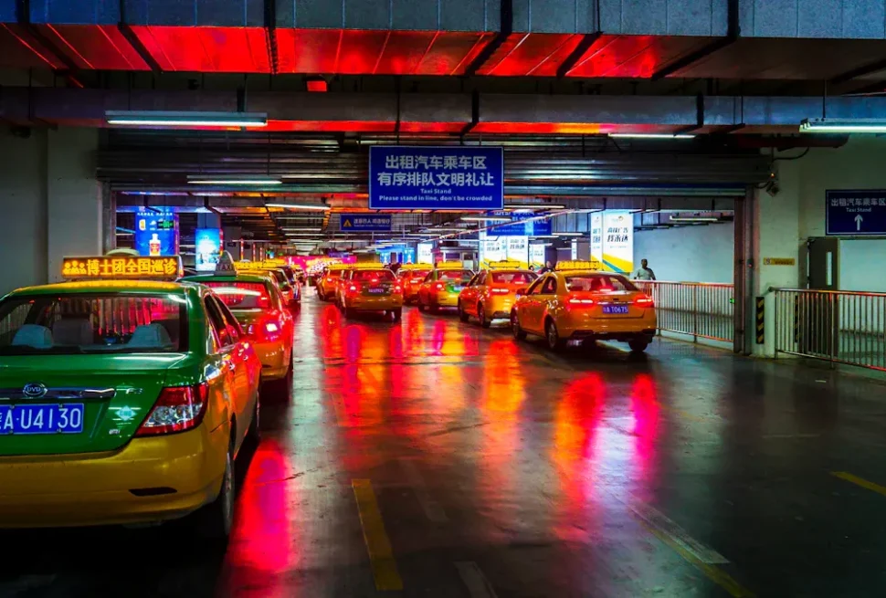 Taxi line in a dim underground parking garage with wet, reflections from red and blue lights on the floor, foreground shows a green taxi
