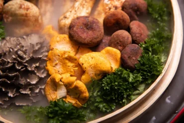 Assorted fried snacks (potato croquettes, chips) and greens in a round dish with parsley garnish, steaming hot.