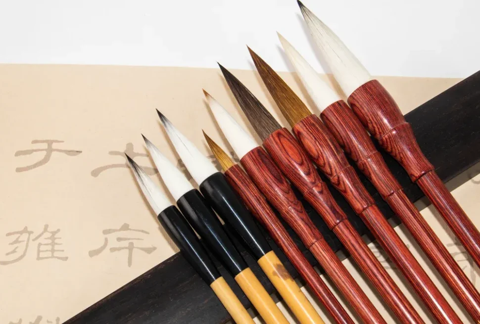 Set of Chinese calligraphy brushes with wood handles laid on parchment with script