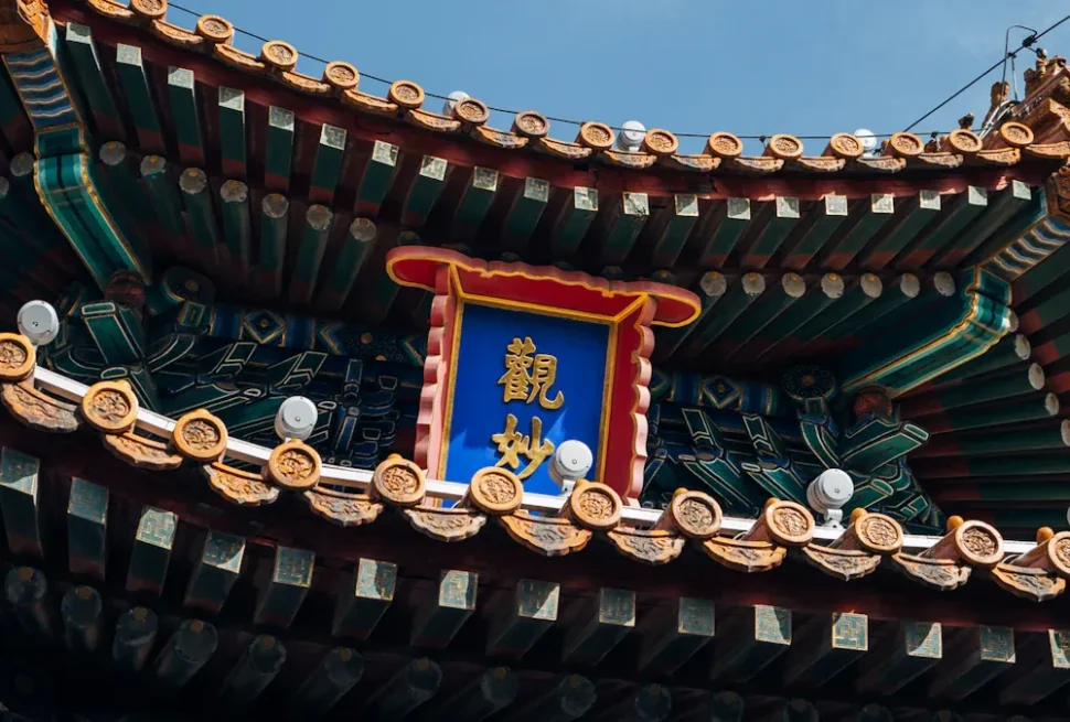 Close-up of an ornate Chinese temple roof with green beams, gold tiles, and a blue plaque bearing gold Chinese characters.