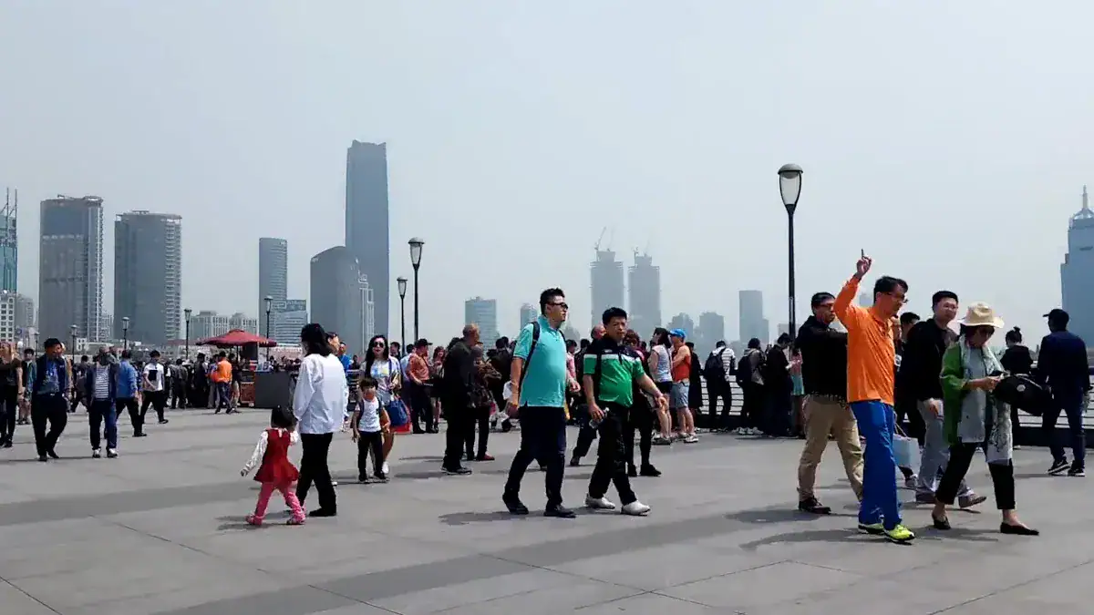 The Bund,Shanghai,Chinatour Crowded waterfront promenade with pedestrians and a distant city skyline of tall buildings on a clear day.