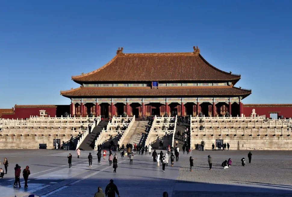 Main hall of the Forbidden City in Beijing with red walls, a golden tiled roof, and visitors on the steps and courtyard.