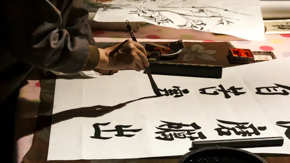 Close-up of a person’s hand holding a calligraphy brush, writing bold black characters on white paper with ink and an ink stone nearby.