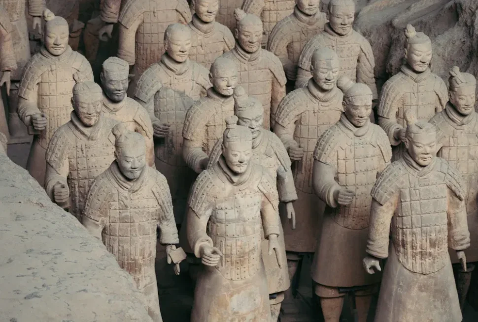 Rows of life-size terracotta soldiers in armor standing in a dusty pit.
