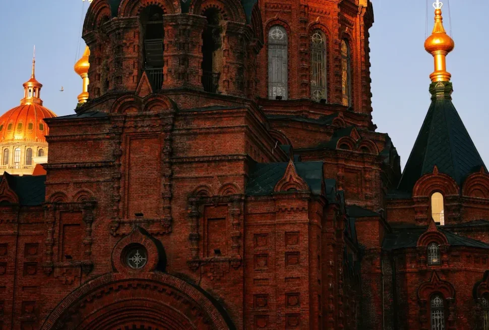Harbin's Culinary,Harbin,Chinatour Red-brick church with ornate arches and a dark roof, gold-domed building visible behind it in the background.