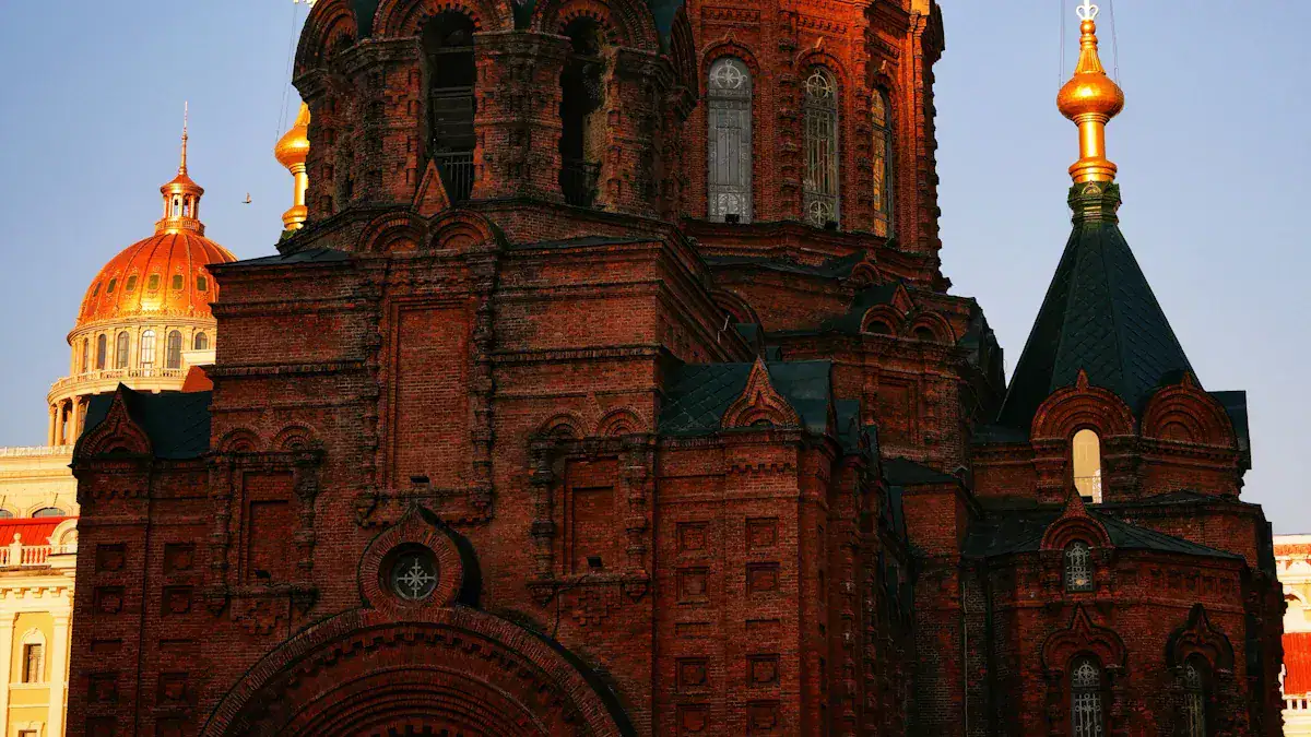 Red-brick church with ornate arches and a dark roof, gold-domed building visible behind it in the background.