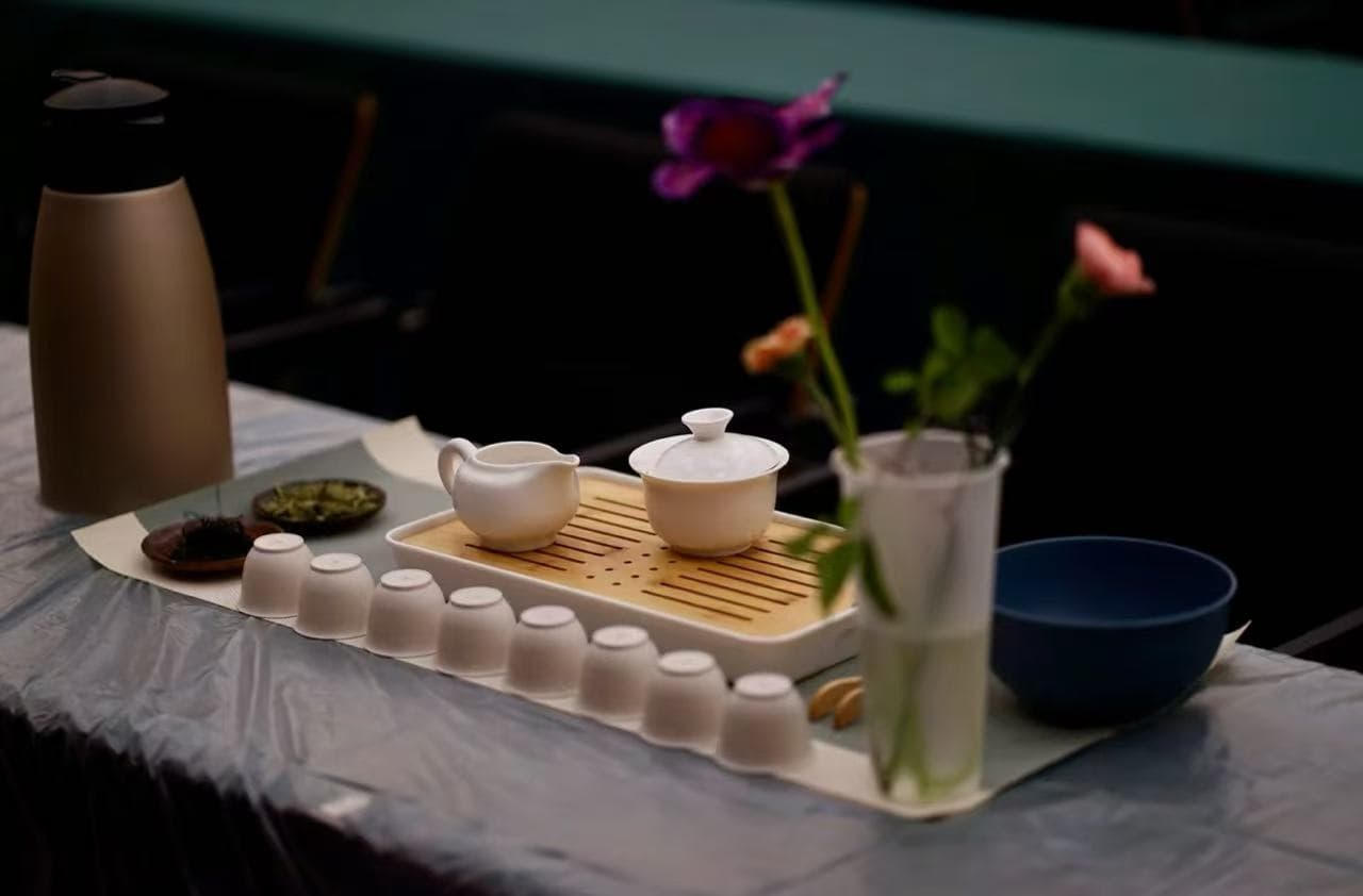 Shanghai Tea Ceremony,Shanghai,Chinatour White ceramic tea set on a tray with a teapot and a row of upside-down cups, on a table with a vase of pink flowers nearby.