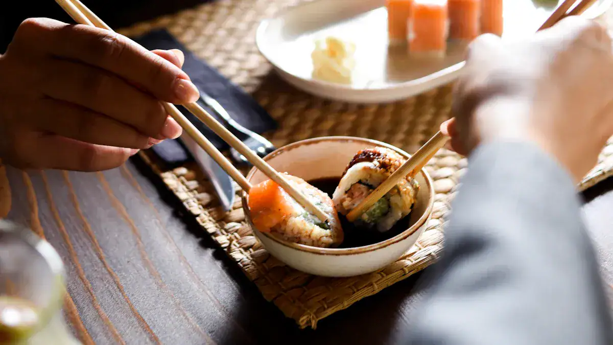 Hands use chopsticks to pick sushi from a small bowl on a woven placemat at a dining table.