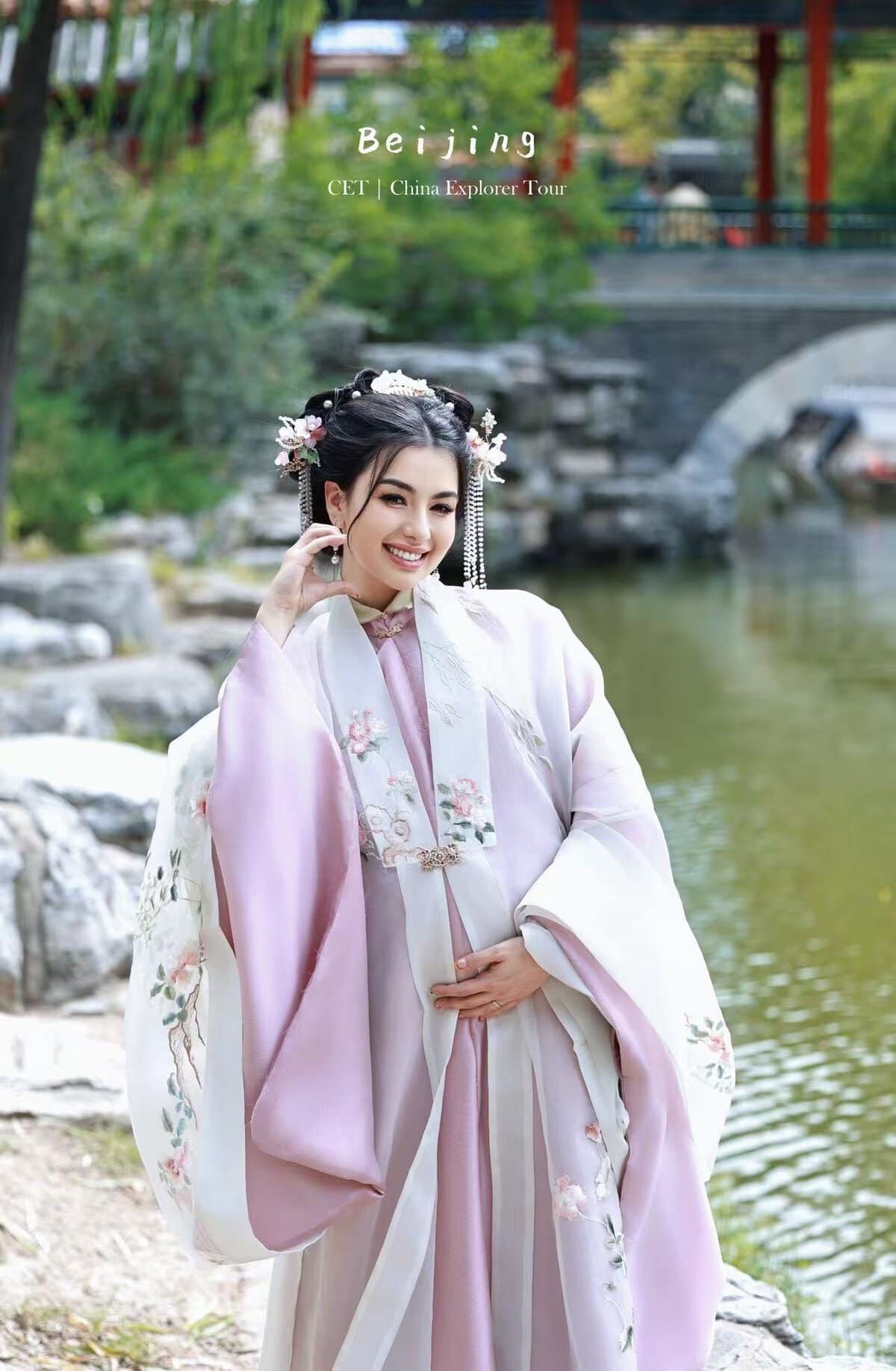 Hanfu Photoshoot, Beijing, Zhongshan park, female, chinatravel, Woman in a pale pink traditional Chinese hanfu posing by a pond with a stone bridge in the background; text reads 'Beijing CET | China Explorer Tour' at top.