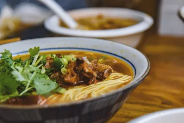 Bowl of beef noodle soup garnished with cilantro and green onions on a wooden table.