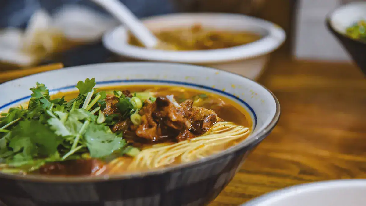Bowl of beef noodle soup garnished with cilantro and green onions on a wooden table.