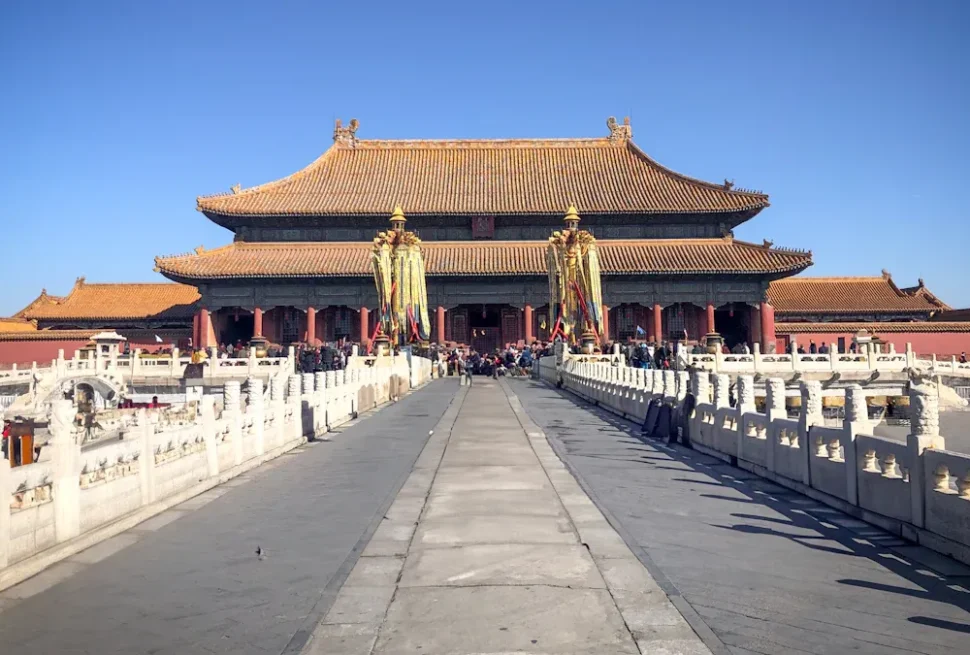Wide stone walkway leads to a grand traditional Chinese imperial hall with yellow-tiled roof and red columns, surrounded by visitors at a historic palace complex.